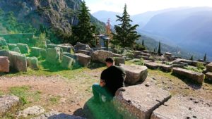 デルフィ遺跡でアポロン神殿を見上げる途中に座る男性の姿
